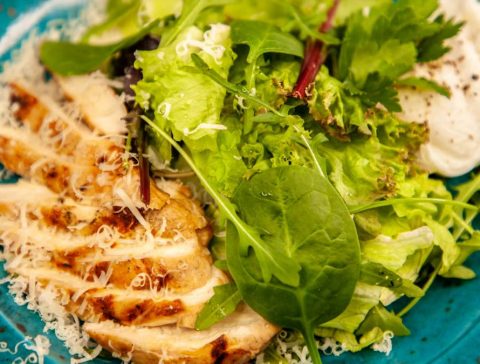 Close-up of a grilled chicken salad with mixed greens and cheese, served on a blue plate.