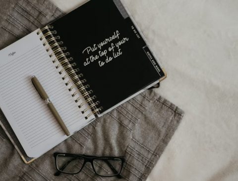Stylish flatlay featuring a planner with quote, pen, and eyeglasses on a neutral background.