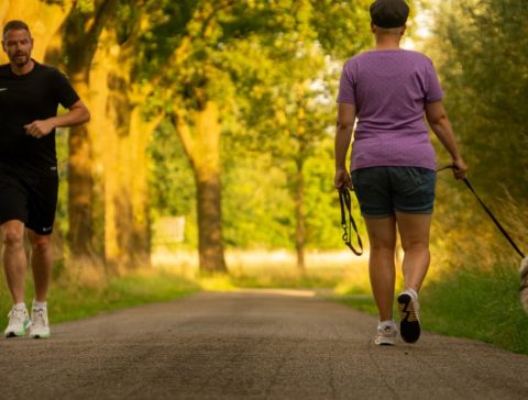 Man jogging and woman walking a dog on a picturesque outdoor path.